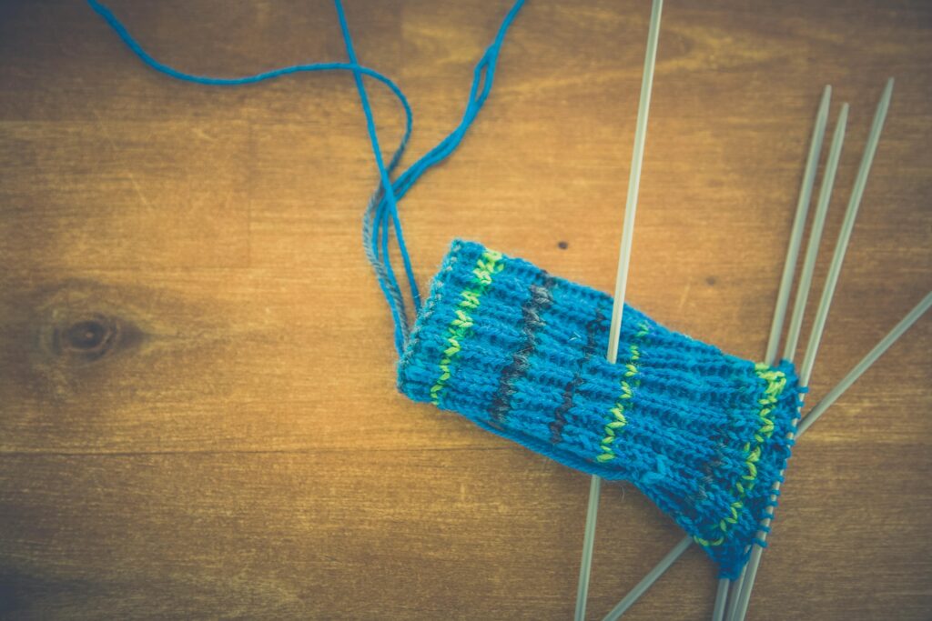 A vibrant knitting project using blue and green yarn with needles resting on a wooden table.